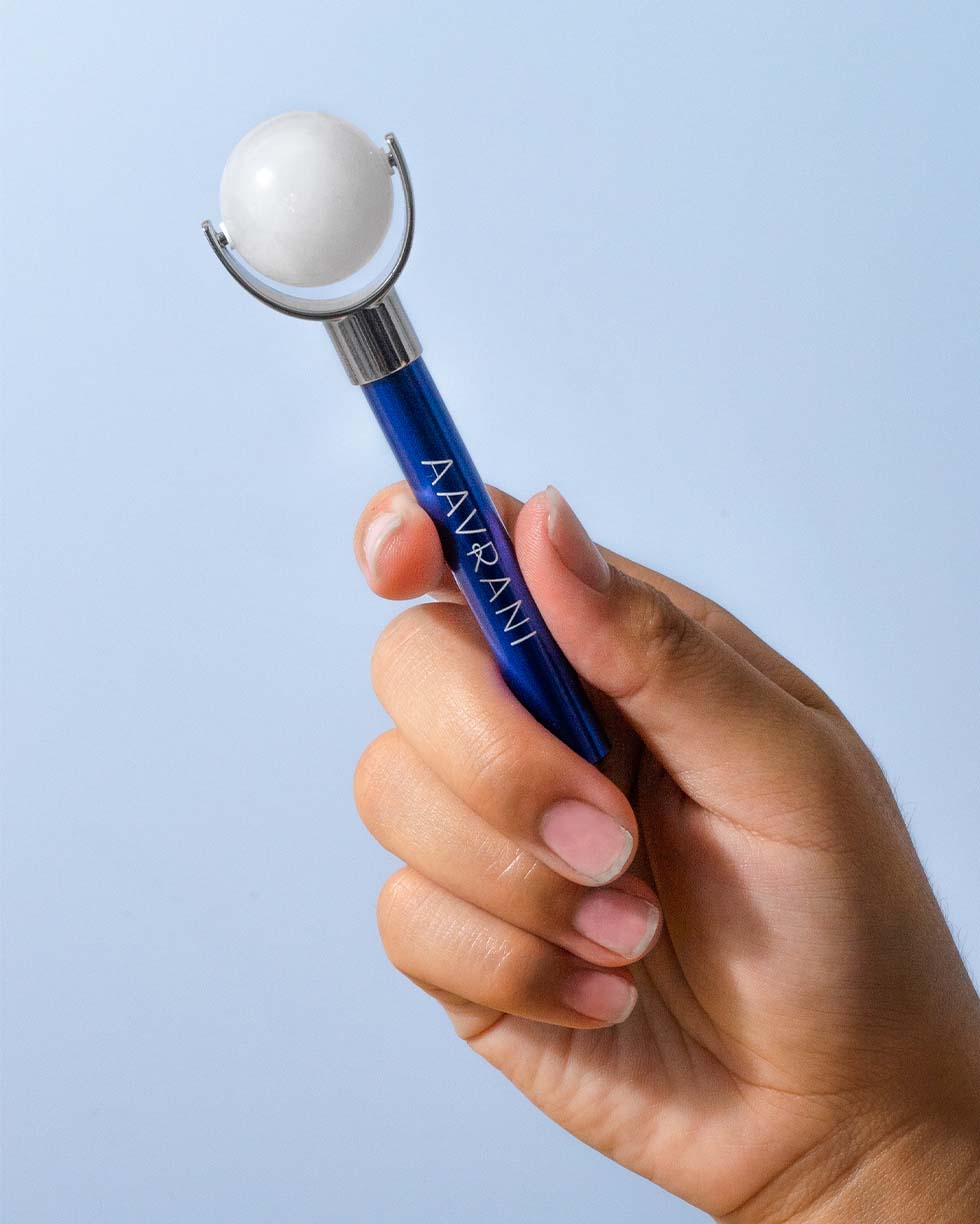 Rollmate Facial Roller being held against blue background